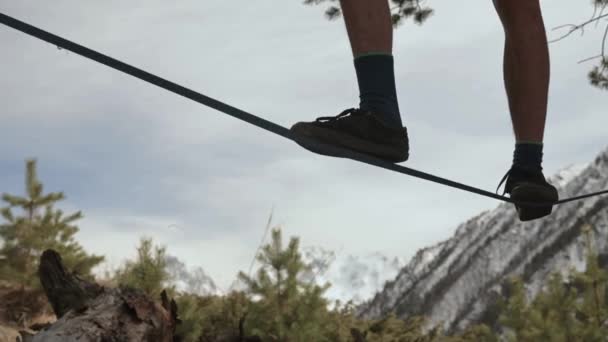 Un joven se tambalea en una línea floja en las montañas del norte del Cáucaso. Primer plano de las piernas de atleta en medio de montañas cubiertas de nieve — Vídeos de Stock