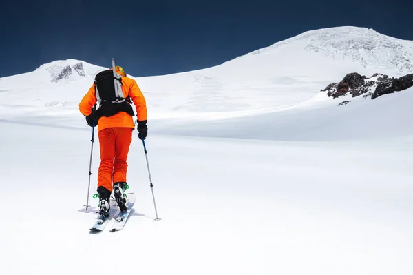 Ascent of a skier with a backpack in a mask and sunglasses on skis with poles to go uphill for freeride and backcountry. North Caucasus. Climbing Volcano Elbrus — Stock Photo, Image