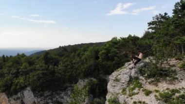 Çekici, uzun saçlı, atletik bir adam bir uçurumun kenarında elinde dron kontrol paneli ile oturuyor. İnsansız hava aracı uçuşları doğa rezervleri ve insansız hava aracı eğlencesi