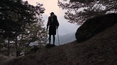 Dağların bulutlu havasında, akşamları ormandan çıkan uzun saçlı genç bir adamın arka görüntüsü. Seyahat ve seyahat.