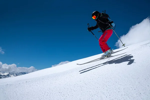 Жінка лижниця-спортсменка робить стрибок у політ на сніжному схилі на тлі блакитного неба гір і хмар. Фрірайд і екстремальне катання на лижах для жінок — стокове фото