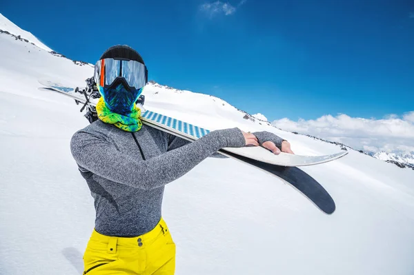 一个身材苗条、身披紧身衣、头戴滑雪面罩、头戴护目镜的女孩站在那里，肩上披着滑雪板 — 图库照片