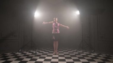 Güzel pembe elbiseli çekici genç kız profesyonel dansçı salon sporu sambu Latin Amerikalı dumanla dolu karanlık bir odada dans ediyor.