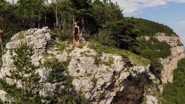 一个身穿黑色T恤和短裤的年轻人站在悬崖边，环顾四周。带岩石和森林的自然保护区的空中景观 — 图库视频影像