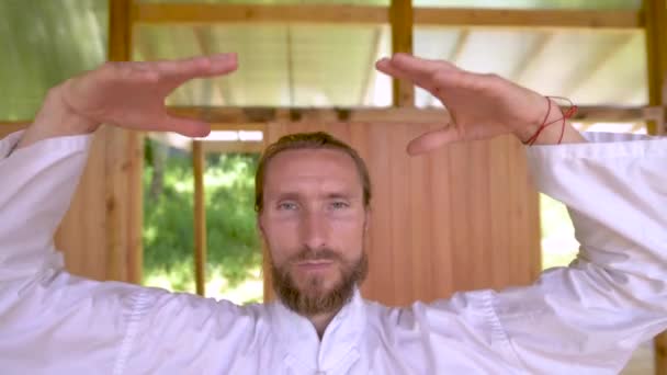 Skäggig kaukasisk man klädd i vita kläder för att träna koncentration och andning innan han tränar qigong tai chi — Stockvideo