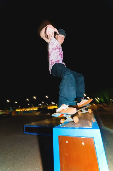 Jovem patinador fazendo truque slide em trilhos no parque de skate à noite — Fotografia de Stock