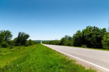 Yazın asfalt yolda yol kenarlarında mavi gökyüzüne karşı yeşil çimenler ve ağaçlar vardı. Ulaşım ve ulaşım lojistik şirketleri için güneşli bir gün.
