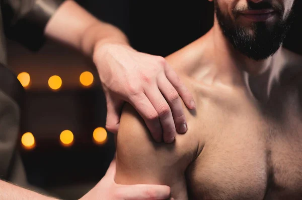 Male masseur doing sports massage in luxury spa salon to male athlete with a beard on the background of burning candles — Stock Photo, Image