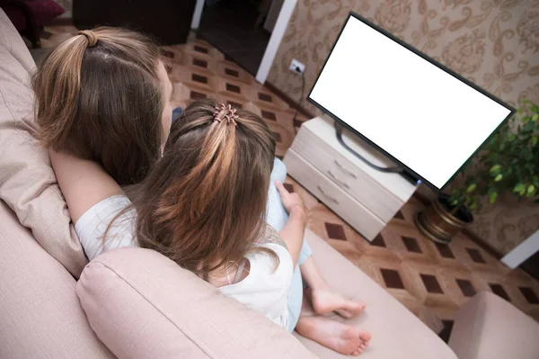 Young family of long haired man and woman are lying on the couch and watching TV. The TV screen is cut out white. Mockup and template for designer layout