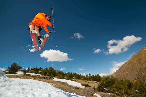 Junger Mann mit Sonnenbrille trickst im Flug mit Schneekicker vor Bergkulisse — Stockfoto