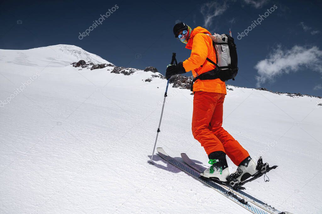 A skier in an orange suit skis in a mountain off-piste skiing in the northern caucasus of Mount Elbrus