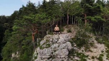 Çekici, uzun saçlı, atletik bir adam bir uçurumun kenarında elinde dron kontrol paneli ile oturuyor. İnsansız hava aracı uçuşları doğa rezervleri ve insansız hava aracı eğlencesi