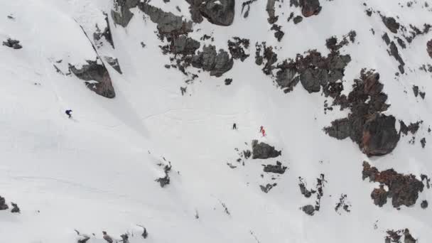 Légi rálátás. Síelők és snowboardosok egy csoportja, magasan a hegyekben, meredek leereszkedésre készül a havas kloir mentén. Sípályán kívüli hivatásos síelés. — Stock videók