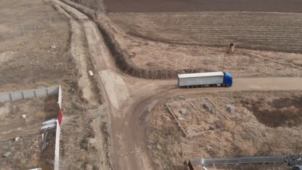 Vista aérea de um grande caminhão com um reboque dirigindo ao longo de uma estrada de terra em busca de um lugar para um U-turn nas proximidades de uma estrada suburbana. — Vídeo de Stock