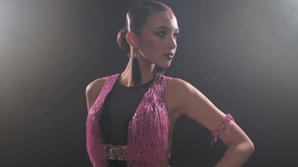 Joven chica atractiva en un vestido de color rosa negro en una habitación oscura con humo está bailando bailes latinoamericanos. Bailarina profesional de baile deportivo de salón 4k — Vídeos de Stock