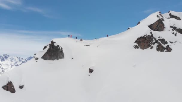 Widok z powietrza. Grupa narciarzy i snowboardzistów, wysoko w górach, przygotowuje się do stromego zjazdu wzdłuż zaśnieżonego couloir. Profesjonalne narciarstwo off-piste. — Wideo stockowe