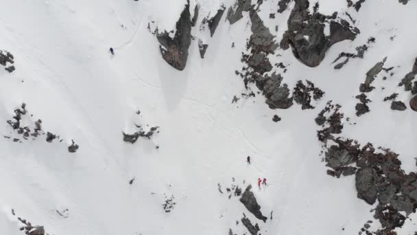 Flygbild. En grupp skidåkare och snowboardåkare, högt uppe i bergen, förbereder sig för en brant nedstigning längs den snöiga kupén. Offpist professionell skidåkning. — Stockvideo