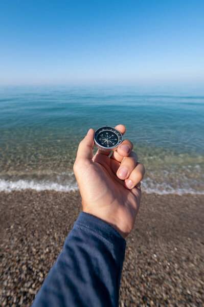 Компас в руке у моря Ман держит магнитный компас на фоне спокойного утреннего моря с дымкой над поверхностью воды
