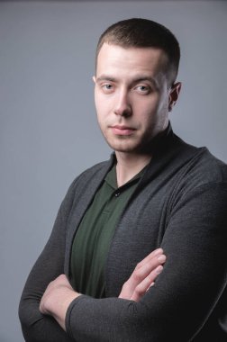 Stüdyo portresi. Sıradan giyinmiş, kolları çaprazlanmış genç bir adam.