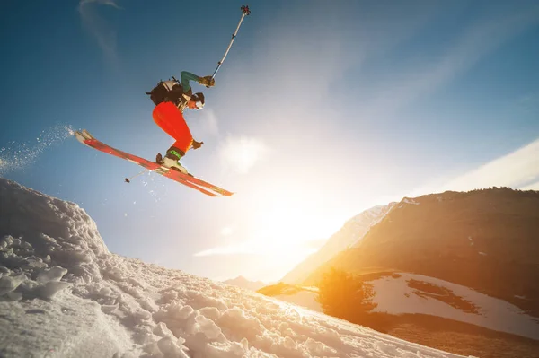 Professionele atleet jonge mannelijke skiër met een rugzak en in een skimasker maakt een truc in de vlucht na het springen van een kicker op de achtergrond van een zonsondergang — Stockfoto