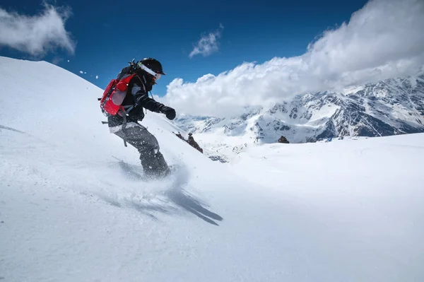 Snowboarder ragazza con uno zaino su un pendio fresco innevato sullo sfondo di alte montagne e cielo blu. Tipi invernali di sport estremi. Snowboard — Foto Stock