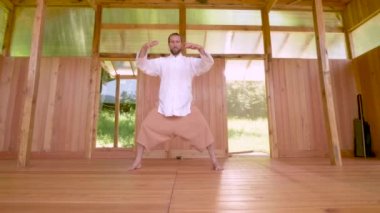 Sakallı, beyaz giysili beyaz bir adam. Qigong Tai Chi çalışmadan önce konsantrasyon ve nefes alma egzersizi yapıyor.