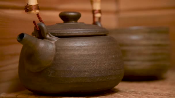 Чайник з глини для чайної церемонії ручної роботи поруч з іншим глиняним посудом на дерев'яній полиці в кімнаті — стокове відео
