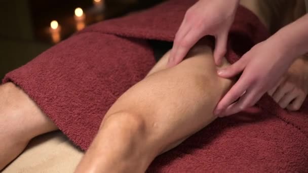 Close-up Masajista masculino haciendo masaje deportivo de los muslos de las piernas a un atleta muscular en una oficina con una luz tenue — Vídeos de Stock