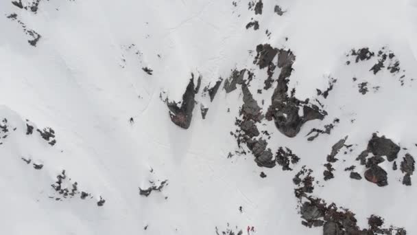 Vista aérea. Un grupo de esquiadores y snowboarders, en lo alto de las montañas, se preparan para un descenso empinado a lo largo del couloir nevado. Esquí profesional fuera de pista. — Vídeos de Stock