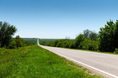 Yazın asfalt yolda yol kenarlarında mavi gökyüzüne karşı yeşil çimenler ve ağaçlar vardı. Ulaşım ve ulaşım lojistik şirketleri için güneşli bir gün.