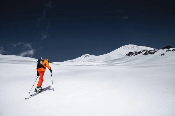 Egy síelő narancssárga öltönyben síel egy hegyen, lesiklópályán kívül, az Elbrus-hegy észak-kaukázusában. — Stock Fotó