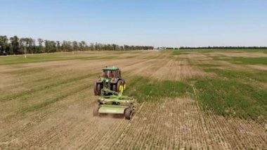 Çim biçme makinesi olan bir traktörün hava görüntüsü boş bir tarladaki çimleri biçer. Yıl boyunca saha hazırlığı ve bakımı