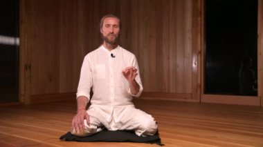 Uzun saçlı adam qigong ve yoga uygulayıcısı lotus pozisyonunda oturup meditasyon salonunun karanlık odasında pratik yapmaktan bahsediyorlar.