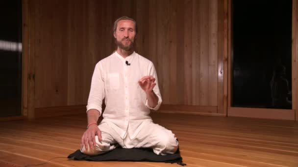 Uzun saçlı adam qigong ve yoga uygulayıcısı lotus pozisyonunda oturup meditasyon salonunun karanlık odasında pratik yapmaktan bahsediyorlar. — Stok video