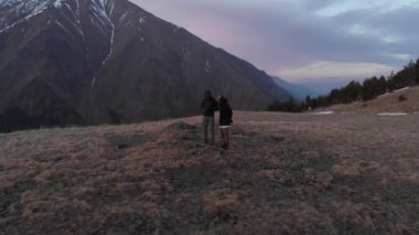 Dağların tepesinde yürüyen ve manzaraya hayran bir kadın ve erkeğin hava manzarası. Dağ sporları yürüyüşü