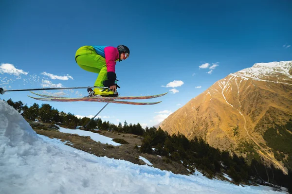 Női síelő sportoló tesz egy ugrás a repülés egy havas lejtőn hátterében kék ég hegyek és felhők. Freeride és extrém síelés nőknek — Stock Fotó
