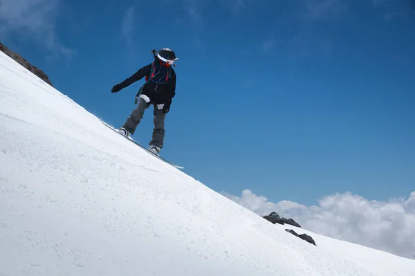 Κορίτσι snowboarder με ένα σακίδιο σε ένα χιονισμένο φρέσκο πλαγιά με φόντο ψηλά βουνά και μπλε ουρανό. Χειμερινά είδη ακραίων σπορ. Snowboard — Φωτογραφία Αρχείου