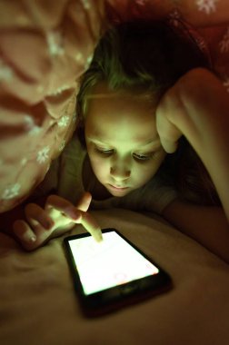 Geceleri yorganın altında akıllı telefonu olan küçük bir kız. Çocukluk aleti bağımlılığı ve uykusuzluk.