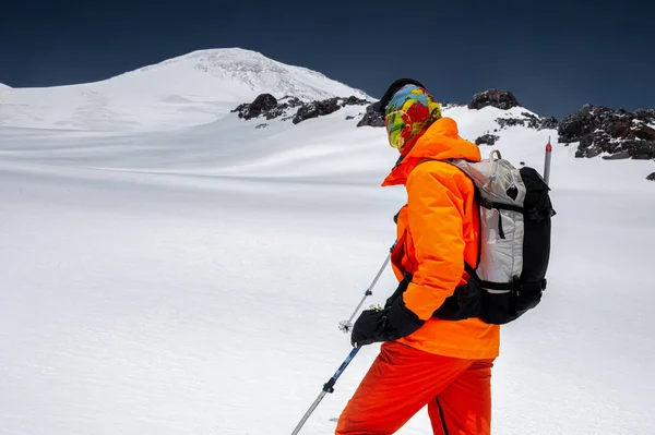 Retrato de um escalador de popa esquiador em óculos de sol e um boné com uma máscara de esqui em seu rosto. contra o pano de fundo do Monte Elbrus — Fotografia de Stock