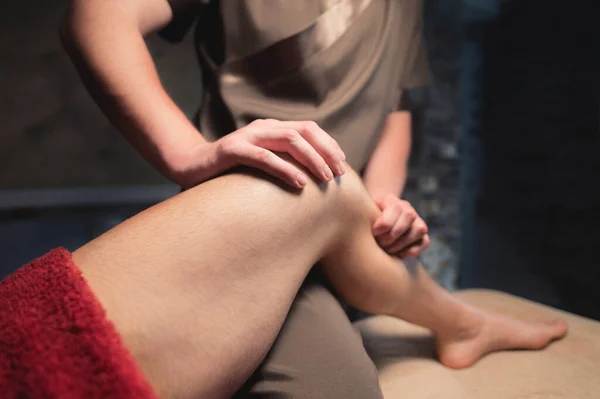 Male massage therapist gives the client a knee and leg massage. Sports massage in a dark room — Stock Photo, Image