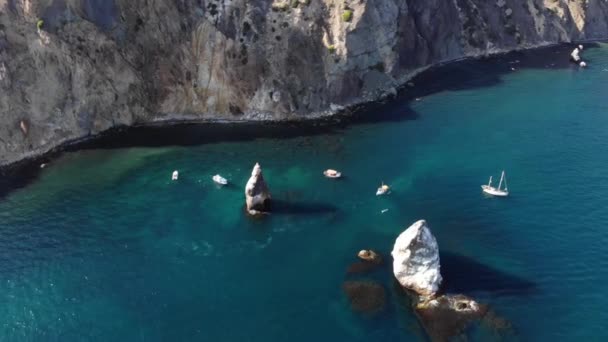 Luchtfoto van de rotskust van de baai met losse rotsen en boten met toeristen die er omheen zwemmen. Turkoois oceaan water in de kuststrook — Stockvideo