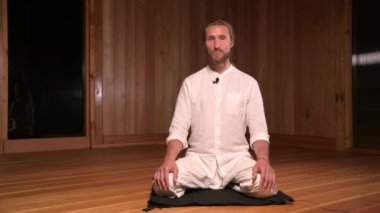Uzun saçlı adam qigong ve yoga uygulayıcısı lotus pozisyonunda oturup meditasyon salonunun karanlık odasında pratik yapmaktan bahsediyorlar.