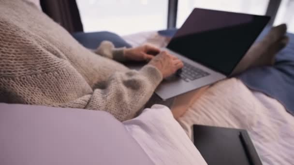 Detailní záběr atraktivní návrhářky na volné noze ve svetru na posteli pracující na notebooku. Vzdálená práce mimo město v zimě — Stock video