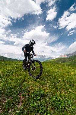 Profesyonel bisikletçi çimenler arasında kayalık bir yolda hızla ilerliyor. Dağlarda ekstrem spor.