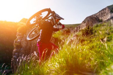 Bir sporcu kayalık bir araziyi bisikletli bir engelle geçer. Ekstrem bir sporcu, bir dağ bisikletiyle dik bir uçuruma tırmanır gün batımının arka planına karşı. Disk dışı kayak.