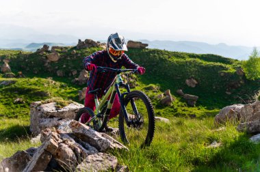 Dağ bisikletçisi kayalık yolda. Erkek bir bisikletçi bisikletini uçuruma itiyor, yürüyerek tırmanıyor. Ekstrem sporlar ve perde arkasındaki hayatları.