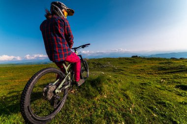 Dağ bisikletinin geniş açılı arka manzarası ve dağların tepelerinde bulutlar ve mavi gökyüzü olan insanlar. Ekstrem spor konsepti, antrenman sırasında rahatlama.