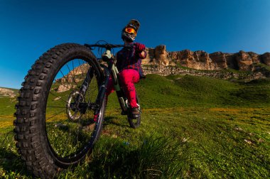 Bisikletli adam maske takıyor ve kaskını takmış tepelerde bisikletinin tepesinde dikiliyor. Dağ bisikleti için yer kopyası. geniş açı