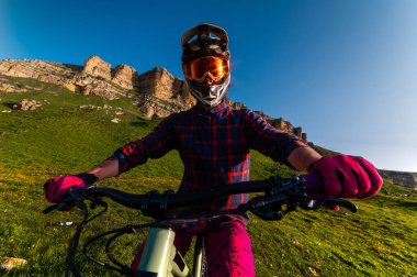 Tam yüz kaskı takmış bir adamın dağlarda bisiklet sürerken açık mavi gökyüzüne bakarken geniş açılı görüntüsü. Profesyonel dağ bisikletçisi..