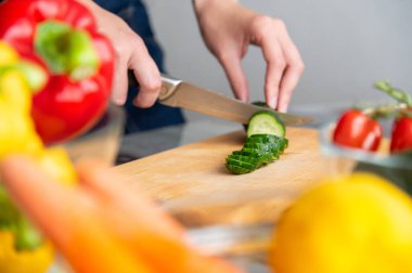 Bir kadın taze bir salatalığı elle keserek salatada pişirmeye hazırlıyor. Sebze doğruyorum. Ev yapımı sağlıklı gıda konsepti.